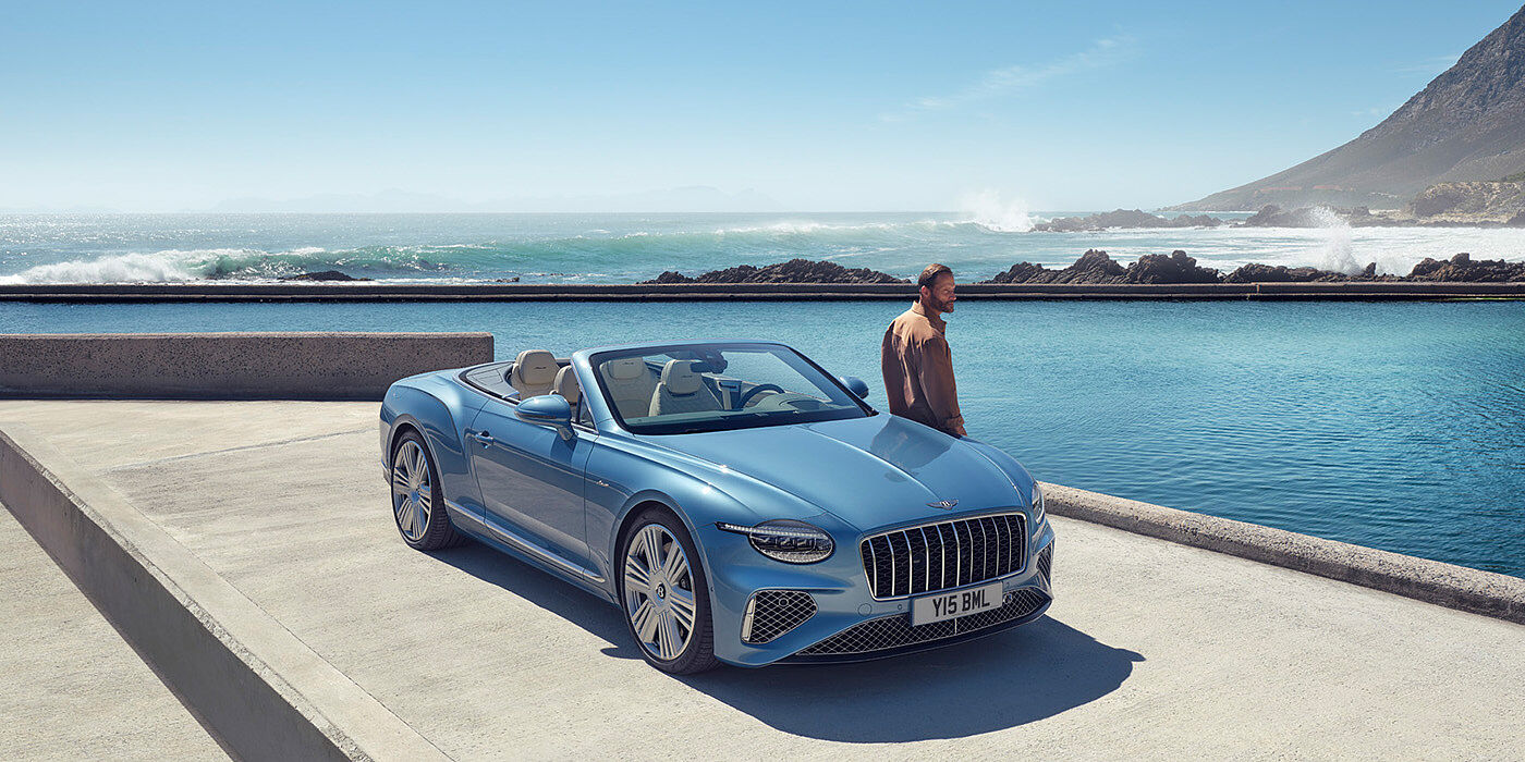 Bentley Brisbane New Bentley Continental GTC Azure convertible front view in Light Windsor blue paint with 22 inch ten spoke wheels parked by the sea in the sunshine