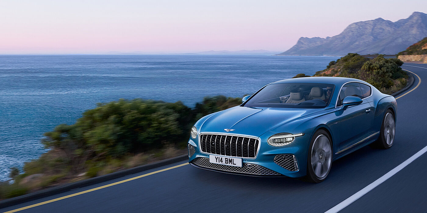 Bentley Brisbane New Bentley Continental GT Azure coupe in Light Windsor blue paint with 22 inch Azure wheels and chrome grill, driving dynamically by the sea