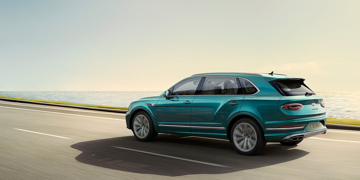 Bentley Brisbane Rear view of a Topaz blue Bentley Bentayga EWB Azure, cruising along a sea side road.