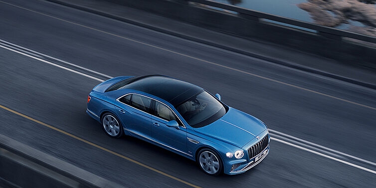 Bentley Brisbane New Bentley Flying Spur Azure sedan in Light windsor blue paint by Mulliner, with 22 inch Azure wheels seen from overhead driving dynamically on a country road