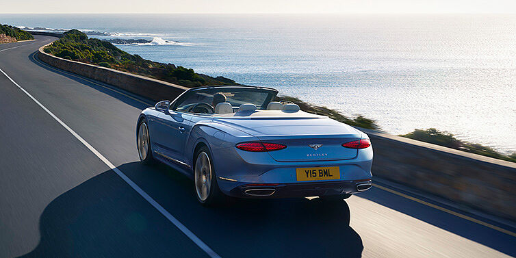 Bentley Brisbane New Bentley Continental GTC Azure convertible rear view in Light Windsor blue paint with 22 inch ten spoke wheels driving dynamically on an ocean road in the sunshine