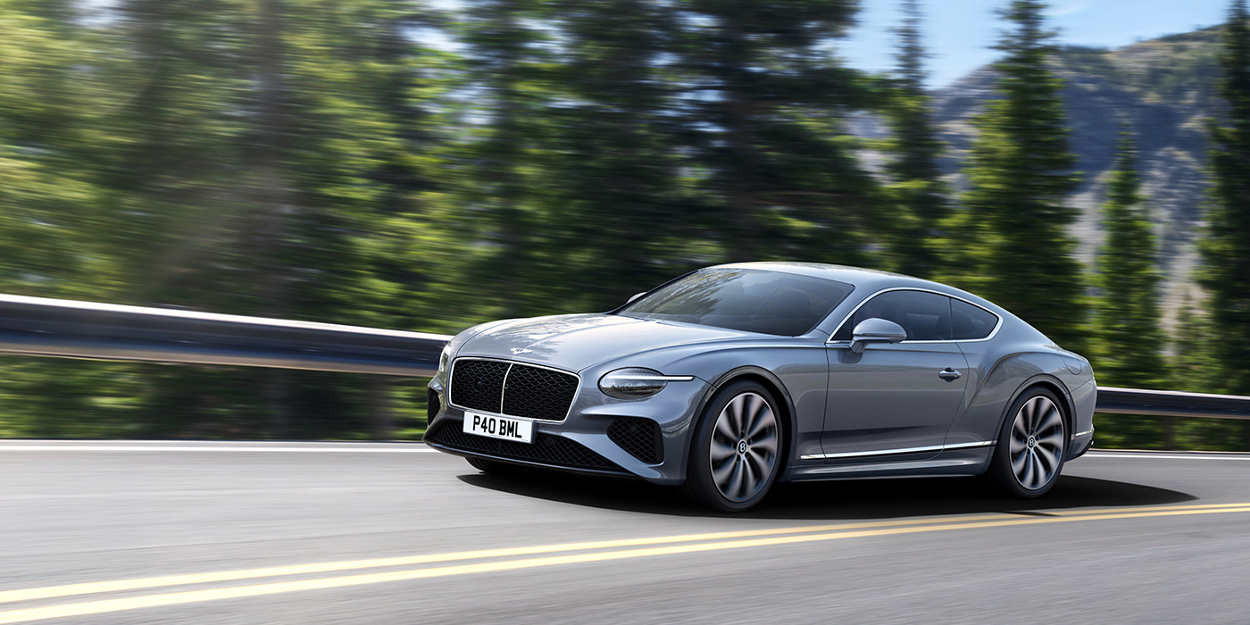 Bentley Brisbane New Bentley Continental GT coupe in Silverlake paint and 22 inch ten-spoke wheels, driving dynamically on a tree-lined road in the sunshine