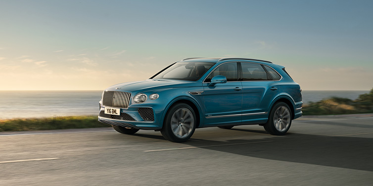 Bentley Brisbane Bentley Bentayga Azure SUV in Topaz blue paint driving dynamically by the ocean with 22 inch 10 spoke directional wheels