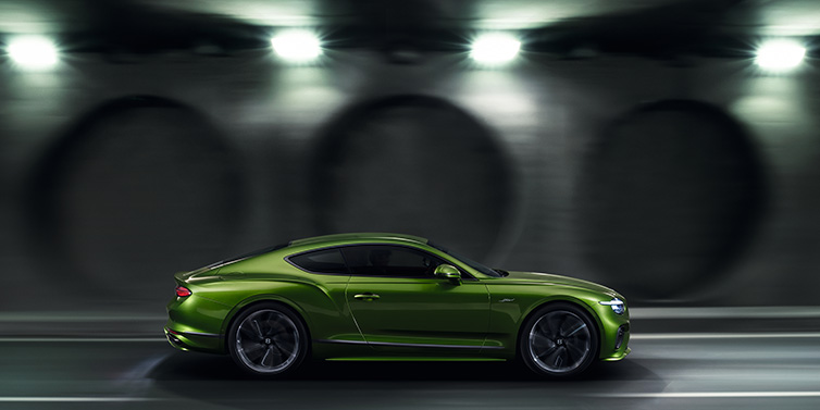 Bentley Brisbane Bentley Continental GT Speed coupe profile in Tourmaline Green driving dynamically past a concrete wall at night