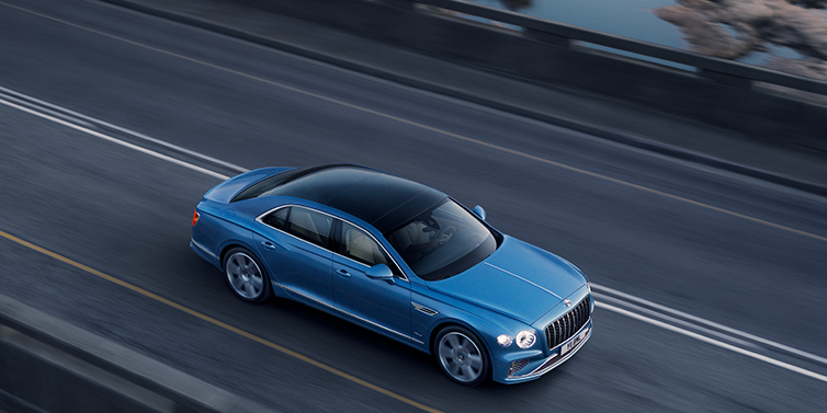 Bentley Brisbane New Bentley Flying Spur Azure sedan in Light windsor blue paint by Mulliner, with 22 inch Azure wheels seen from overhead driving dynamically on a country road