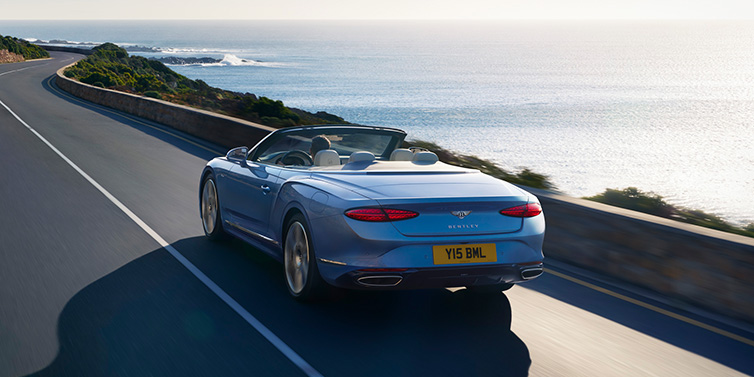 Bentley Brisbane New Bentley Continental GTC Azure convertible rear view in Light Windsor blue paint with 22 inch ten spoke wheels driving dynamically on an ocean road in the sunshine