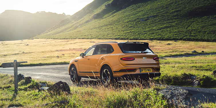 Bentley Brisbane Bentley Bentayga S SUV rear three quarter in Sunburst Gold paint on a road surrounded by green hills