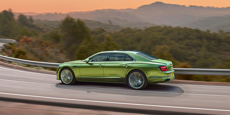 Bentley Brisbane Bentley Flying Spur Speed sedan side profile in Tourmaline Green paint driving dynamically on a mountain road at sunset